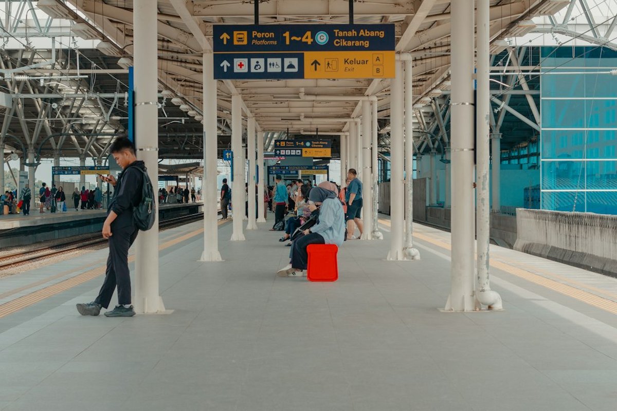 voyageurs sur un quai de gare avec panneau d'affichage