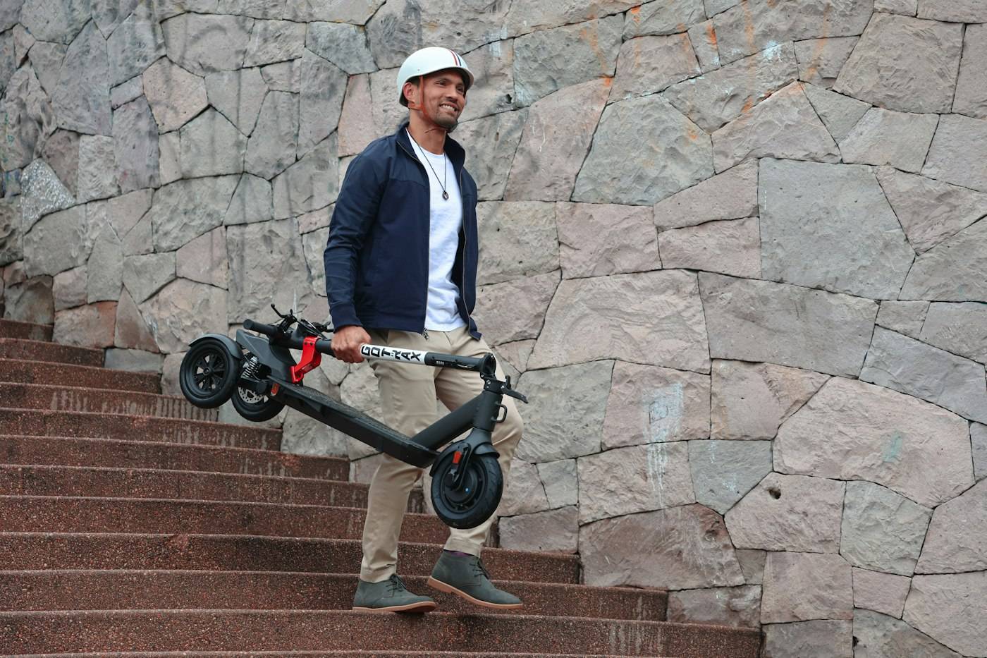 Homme portant une trottinette électrique pliée dans un escalier